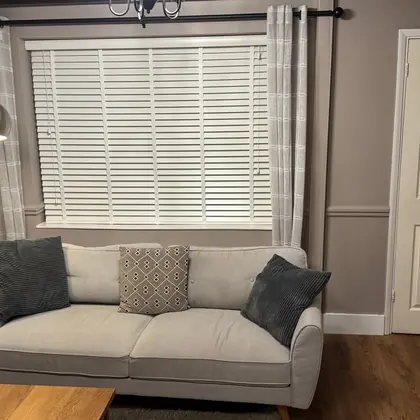 A wide wooden venetian blind fitted above a sitting room sofa